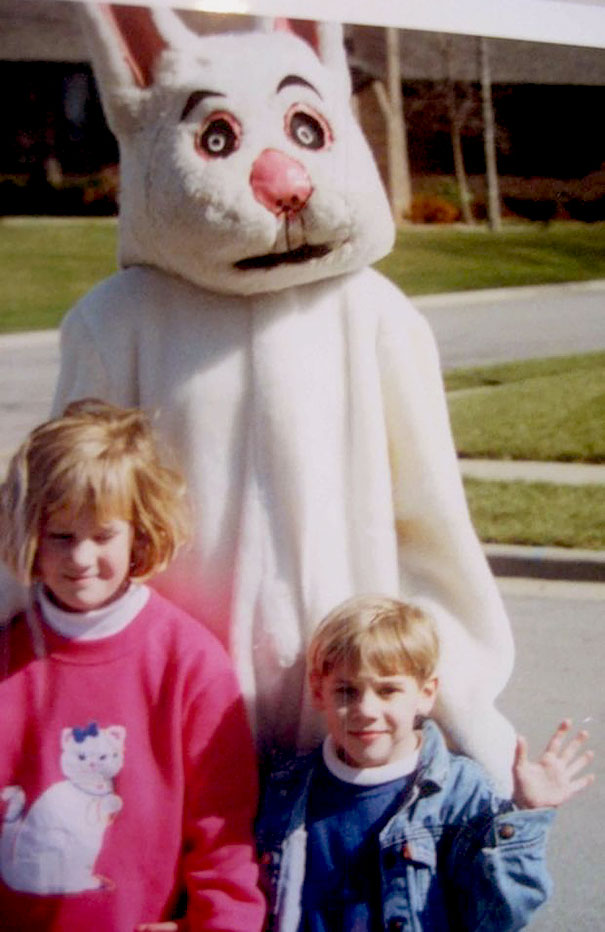 A imagem mostra um coelhinho da Pascoa em tamanho humano envolvendo uma criança nos braços